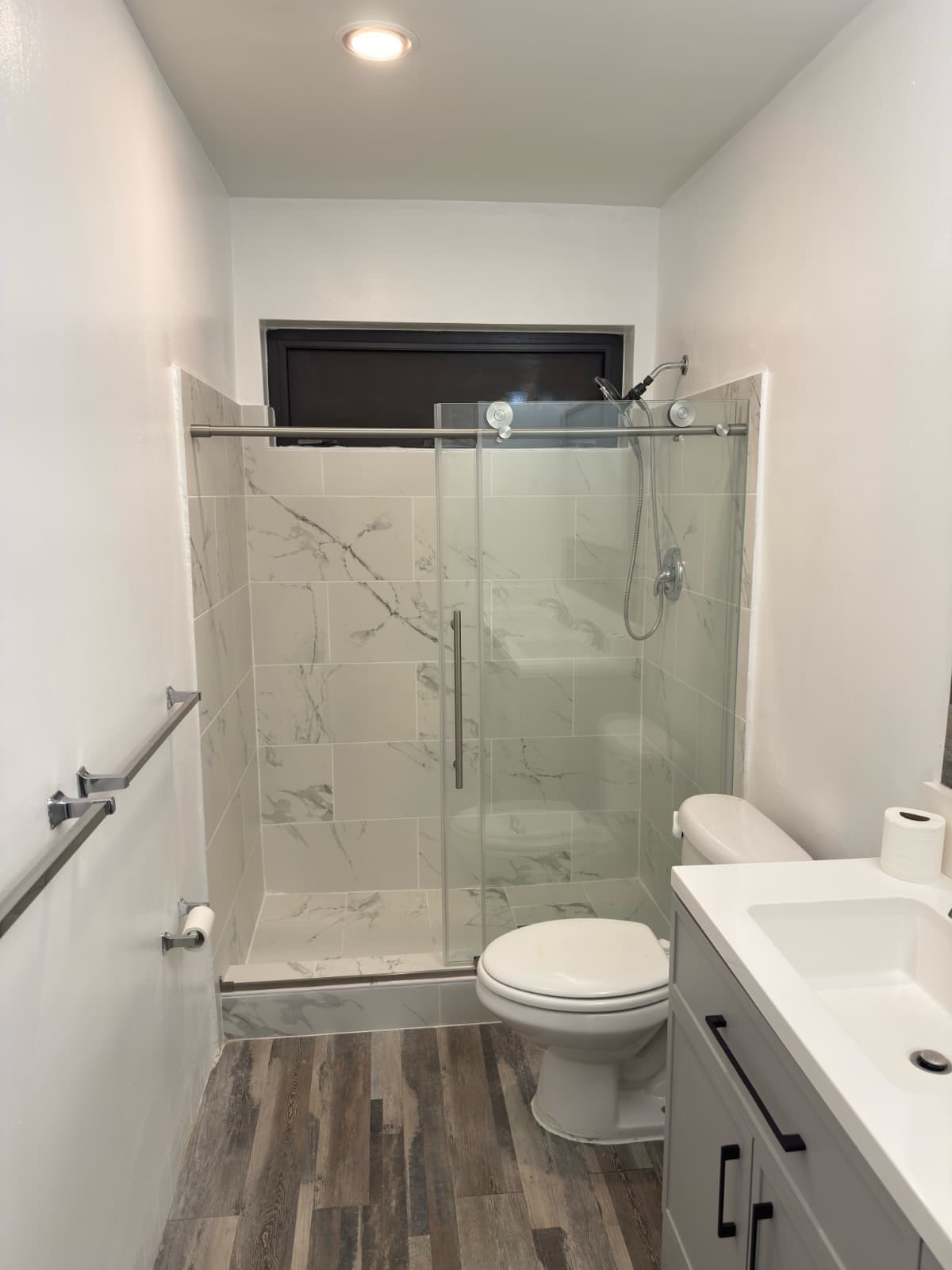 Tub to shower conversion in Killian with a sliding glass door, marble look porcelain tile and a handheld shower on a slide bar