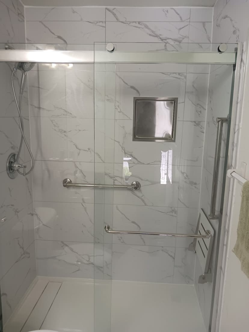Low-threshold shower with grab bars, a tiled niche and sliding glass.