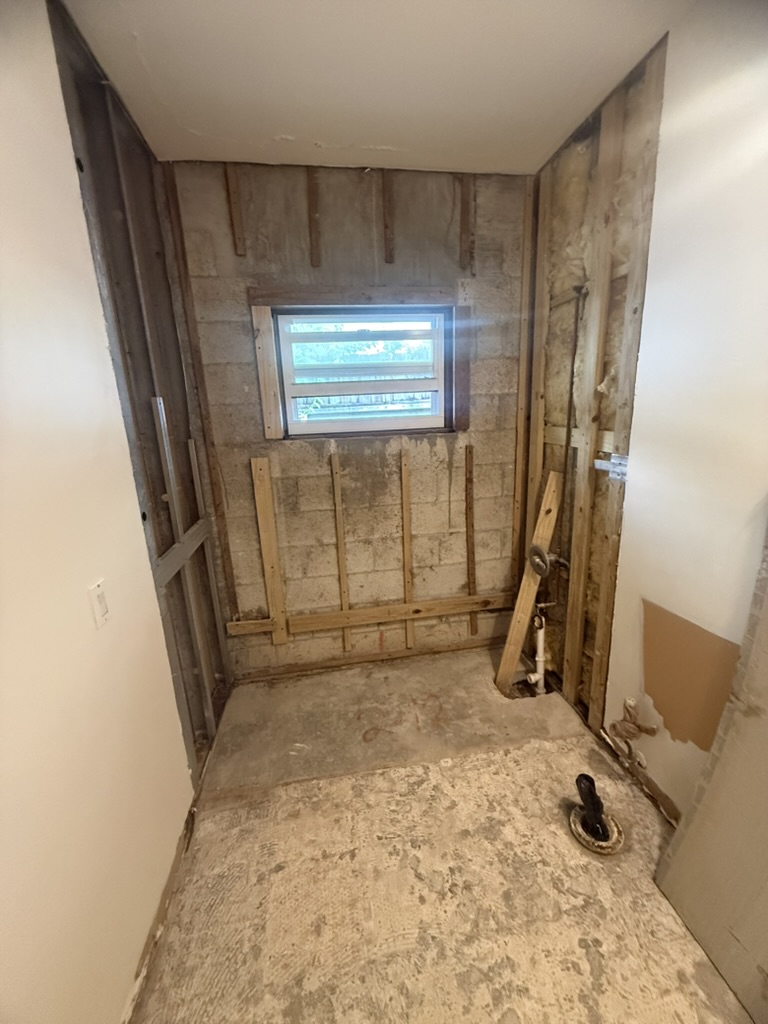 Pared del baño abierta después de sacar la tina, con la estructura y el desagüe expuestos